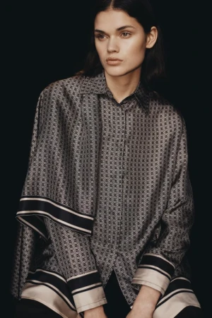 Model wearing a patterned silk shirt with striped cuffs against a dark background, styled by Nisha Van Berkel
