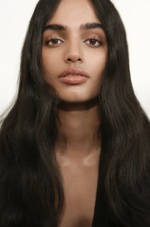 Close-up portrait of a woman with long dark wavy hair and natural makeup against a white background