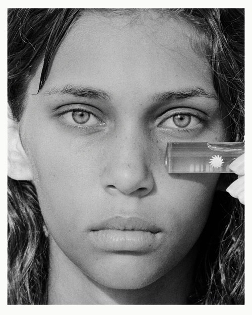 Close-up monochrome portrait of a young woman holding a small glass prism near her eye, photographed by Ryan Brabazon.