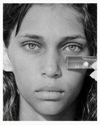 Close-up monochrome portrait of a young woman holding a small glass prism near her eye, photographed by Ryan Brabazon.