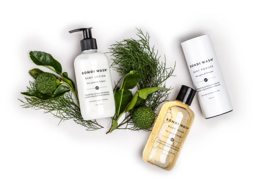 Three Bondi Wash baby care products, including lotion, wash, and powder, displayed with green leaves on a clean white surface.