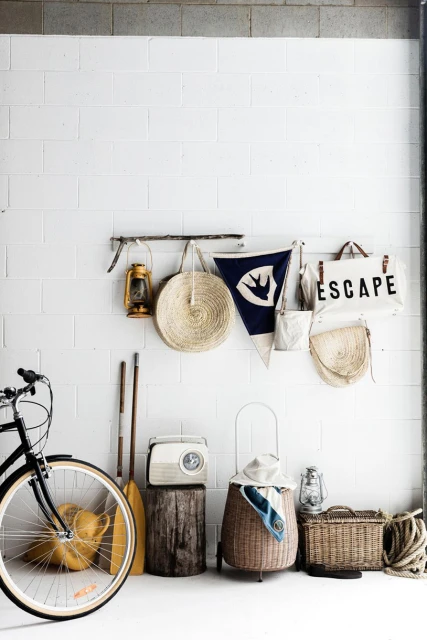 Indoor still life features a bicycle, lanterns, oars, and nautical-themed props against a white brick wall in a natural light setting.