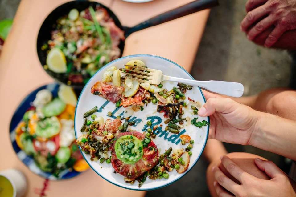 Overhead shot of a plate of leftover food held by a person, including potatoes, meat, and green beans, along with other dishes.