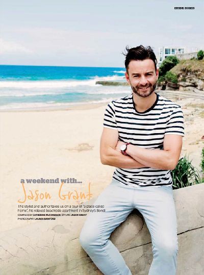 Outdoor portrait of a man in a striped shirt, arms crossed, with a sandy beach and ocean waves in the background on a sunny day.