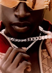 Close-up portrait of a Black man wearing oversized sunglasses and diamond chain necklaces, styled by Kim Payne.