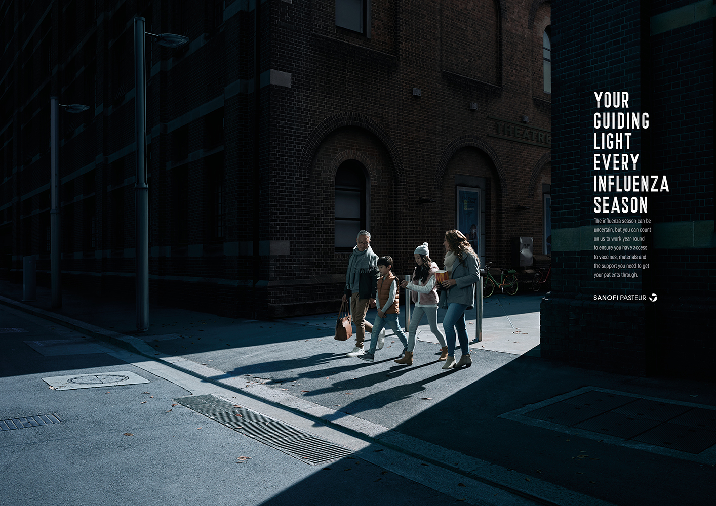 Family of four crossing the street on a sunny day, brick building in the background, promoting influenza season healthcare.