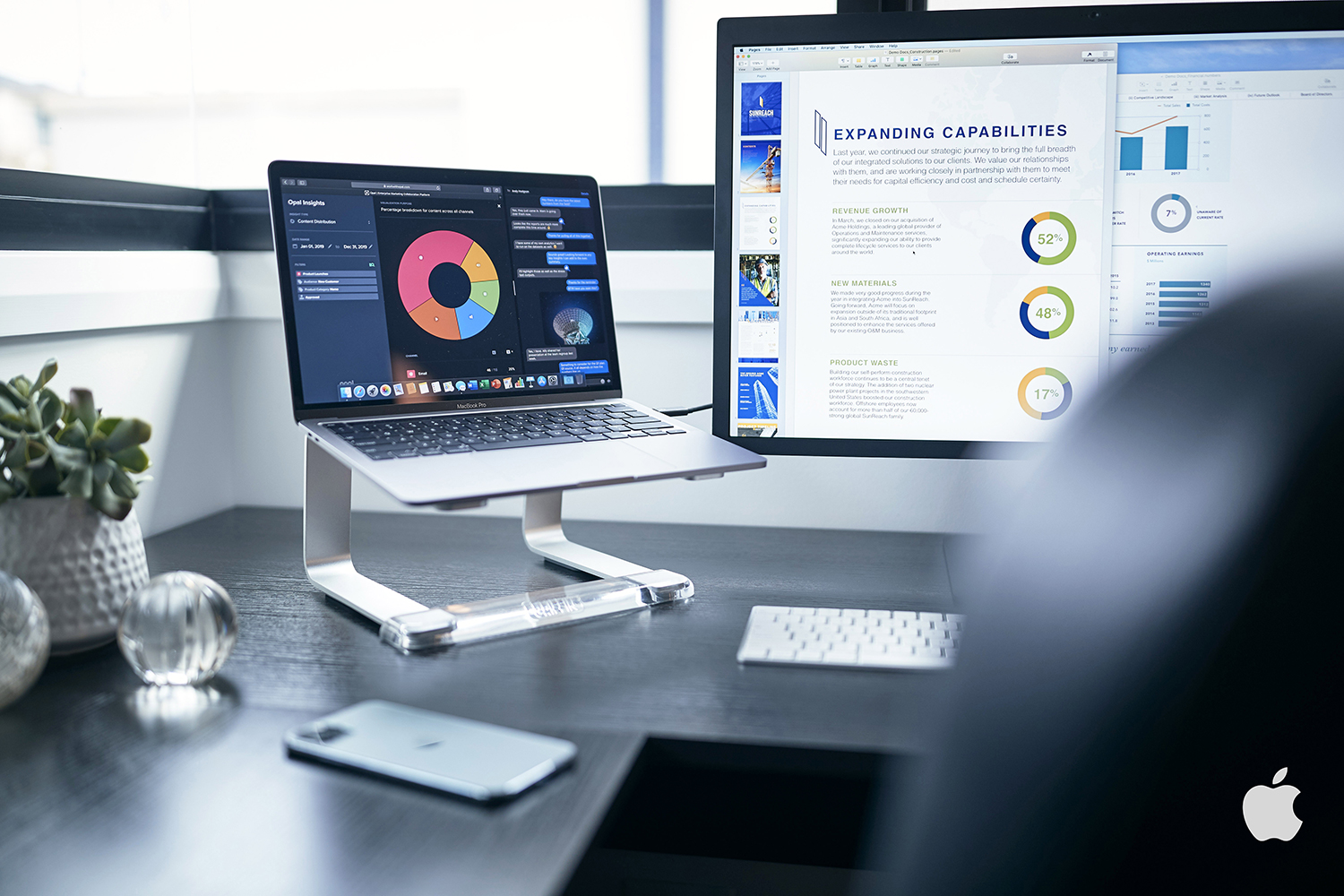 Laptop with a colorful chart displayed on screen, a computer monitor showing data, and a smartphone on a black wooden desk.