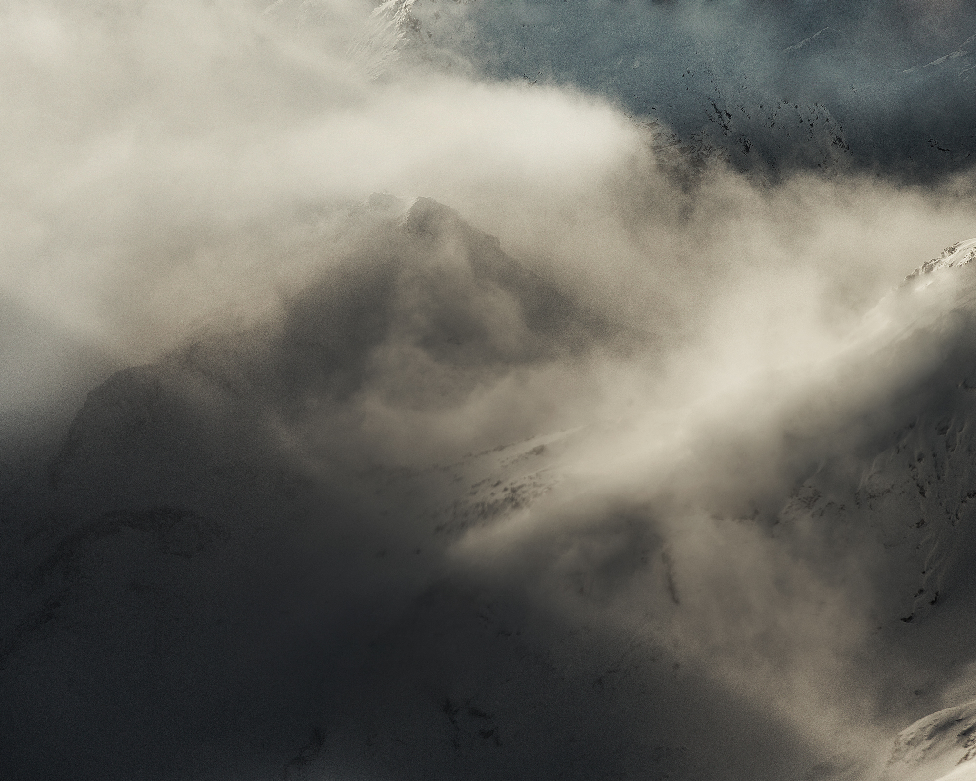 Misty mountain landscape featuring a snow-covered peak shrouded in clouds, creating a moody and atmospheric scene.