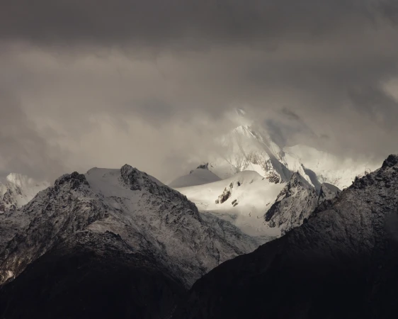 Snow-covered mountains are partially obscured by dark, ominous clouds in this outdoor landscape shot, showcasing a winter scene.