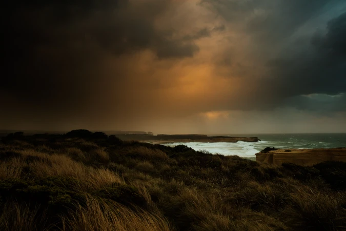 Dramatic coastal landscape with grassy dunes, rocky cliffs, and stormy skies, showcasing moody, natural beauty on the shoreline.