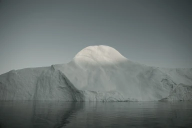 A massive white iceberg floating in dark water under an overcast sky, captured in a horizontal landscape shot by Simon Harsent.