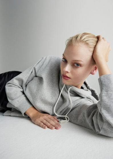 Woman with blonde hair poses in a grey hoodie indoors. Head and shoulders shot.