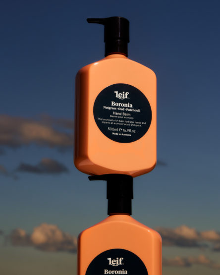 Two stacked peach-colored pump bottles against a blue sky with scattered clouds, advertising Leif Boronia hand balm from Australia.