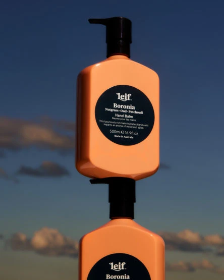Two stacked peach-colored pump bottles against a blue sky with scattered clouds, advertising Leif Boronia hand balm from Australia.