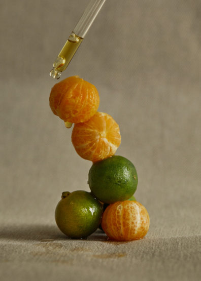 Stacked mandarins and limes are topped with a dropper dispensing liquid, creating a visually striking image.
