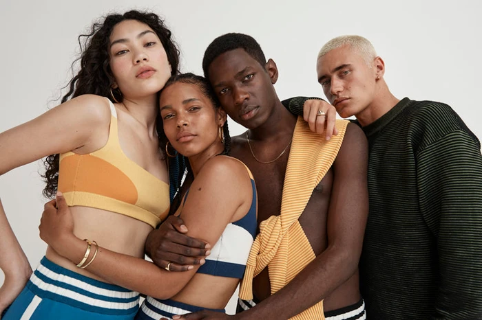 Four diverse models posing closely together against a white background, wearing casual and knit apparel.