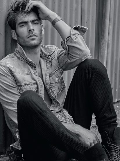 Black-and-white portrait of a handsome adult male fashion model, wearing a denim jacket, posing and looking away from the camera.