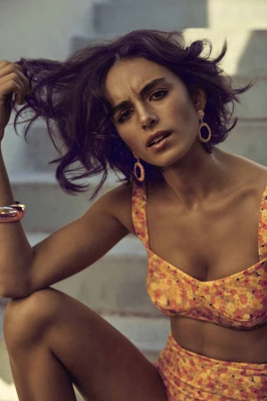 Woman in floral bikini holding her dark hair, wearing hoop earrings, posed outdoors against concrete stairs, photographed by Karima Asaad.