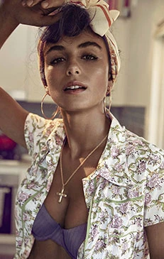 Close-up studio shot of a brunette woman wearing a floral top, bra, cross necklace, and headscarf, looking at the camera with a neutral expression.