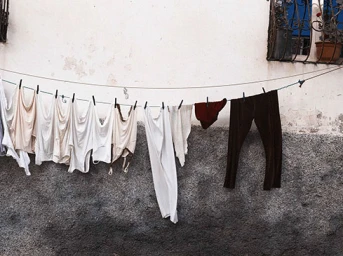 Clothesline with white garments and dark trousers hung against a textured stucco wall