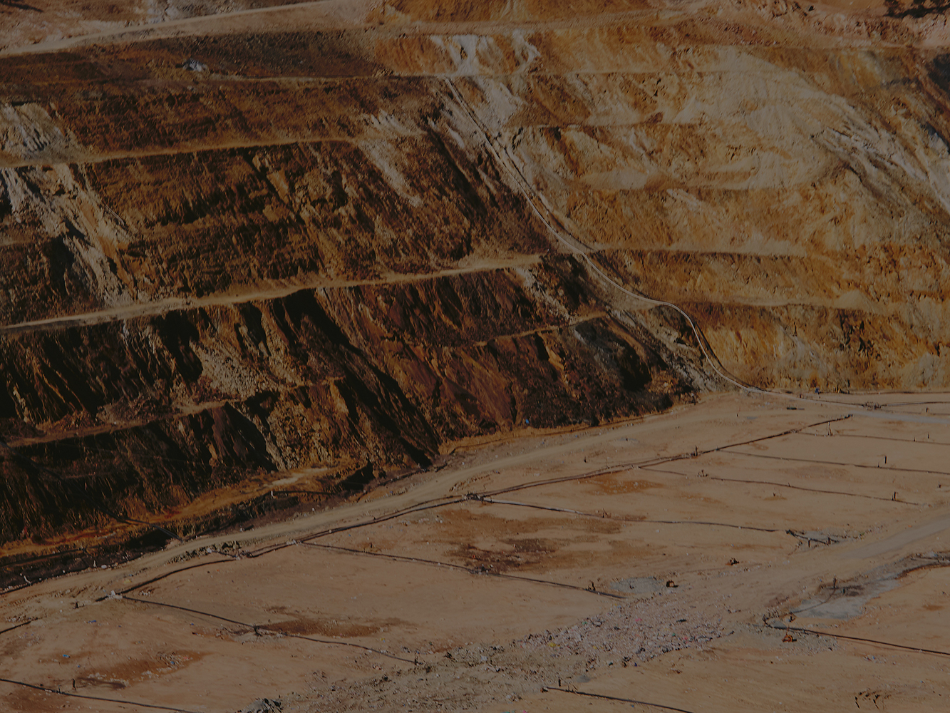 Open-pit mine landscape with terraced walls in earth tones. Mining site shows land degradation and tiered landscape in a sunny environment.