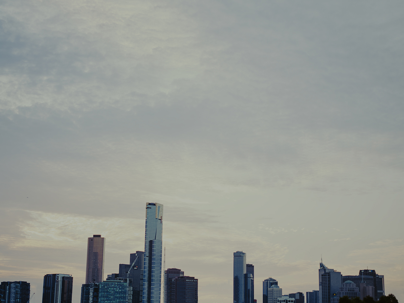 Cityscape featuring modern skyscrapers against a cloudy sky. The urban skyline dominates the lower portion of the frame in overcast weather.