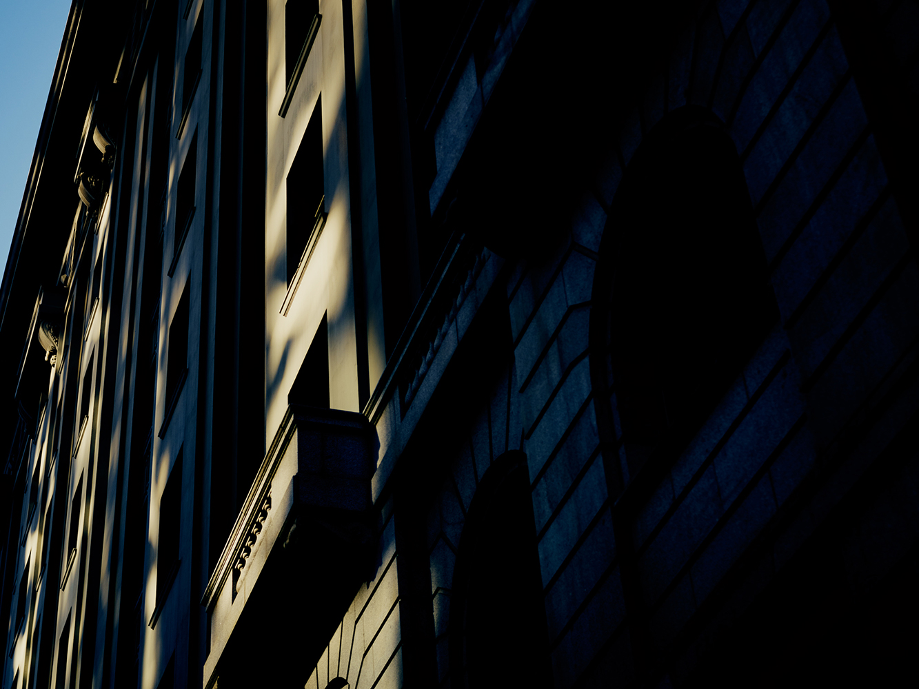 Low angle view of a dark colored building featuring symmetrical rows of windows, architectural detail, and strong contrast.