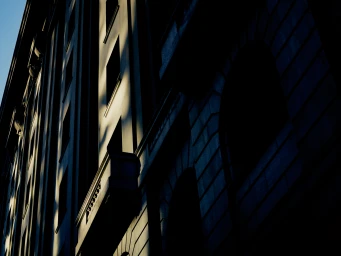 Low-angle architectural photograph of a classic building facade with dramatic shadows and golden sunlight highlights.