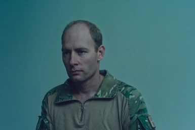 Portrait of a man in camouflage jacket with a serious expression against a plain teal-toned wall in Sydney