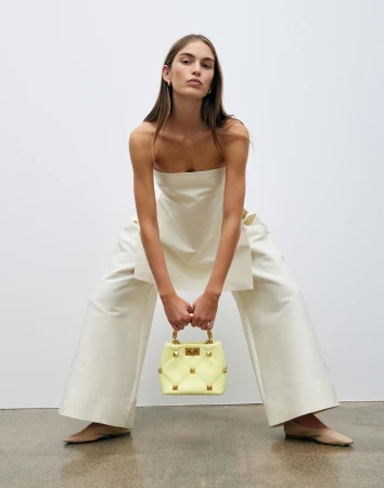Fashion shoot featuring a woman in a light-yellow strapless top and trousers, holding a light-yellow studded handbag indoors.