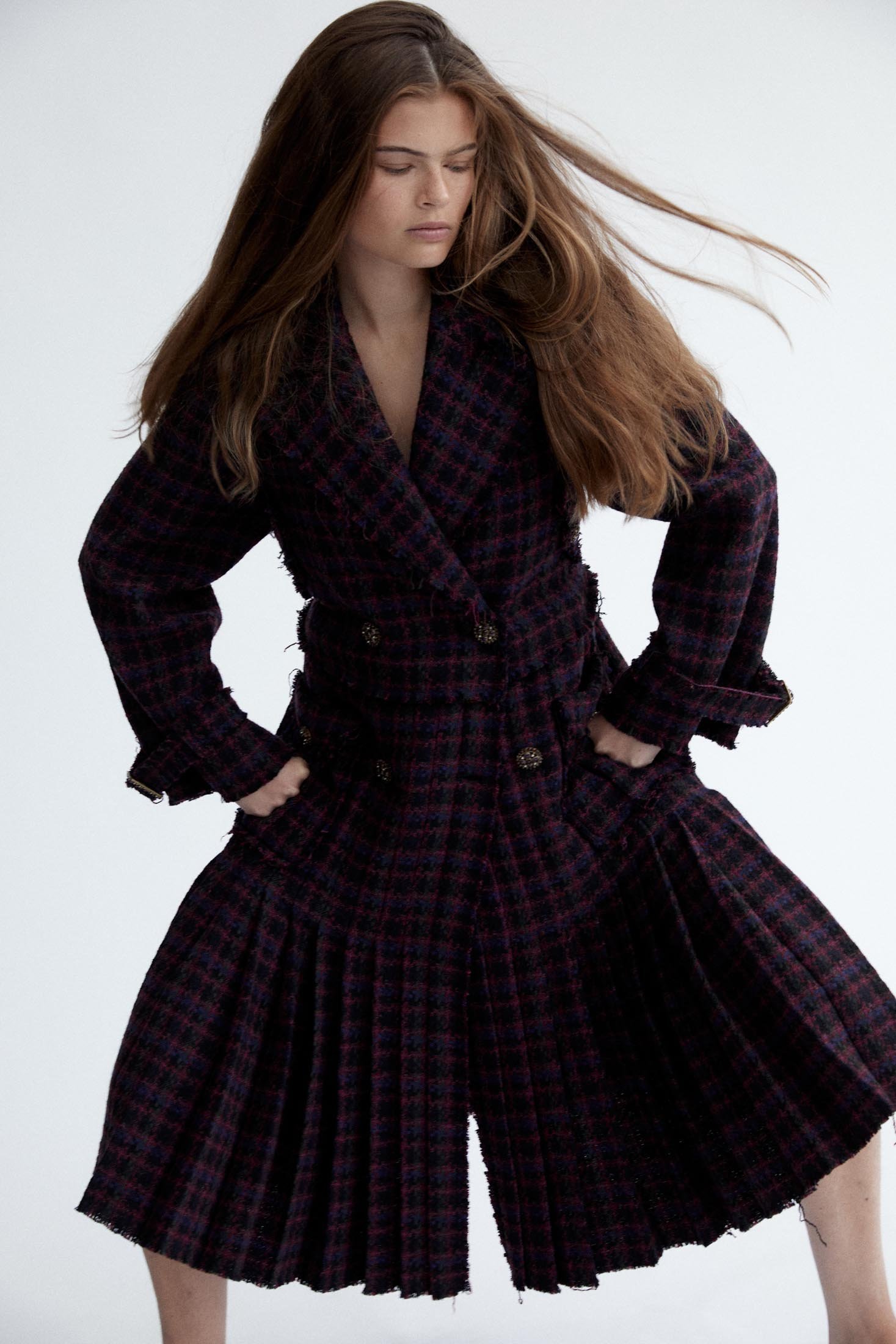 Fashion model wears a tweed coat-dress with pleats in a studio shot against a white background, showcasing the coat's texture and design.