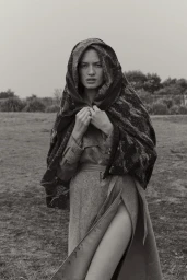 Model in hooded patterned scarf and belted coat standing in grassy field styled by Anastacia Bijou