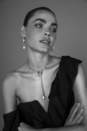 Monochrome portrait of a woman wearing an off-shoulder black dress with pearl drop earrings and a link necklace, styled by Angie Barton.