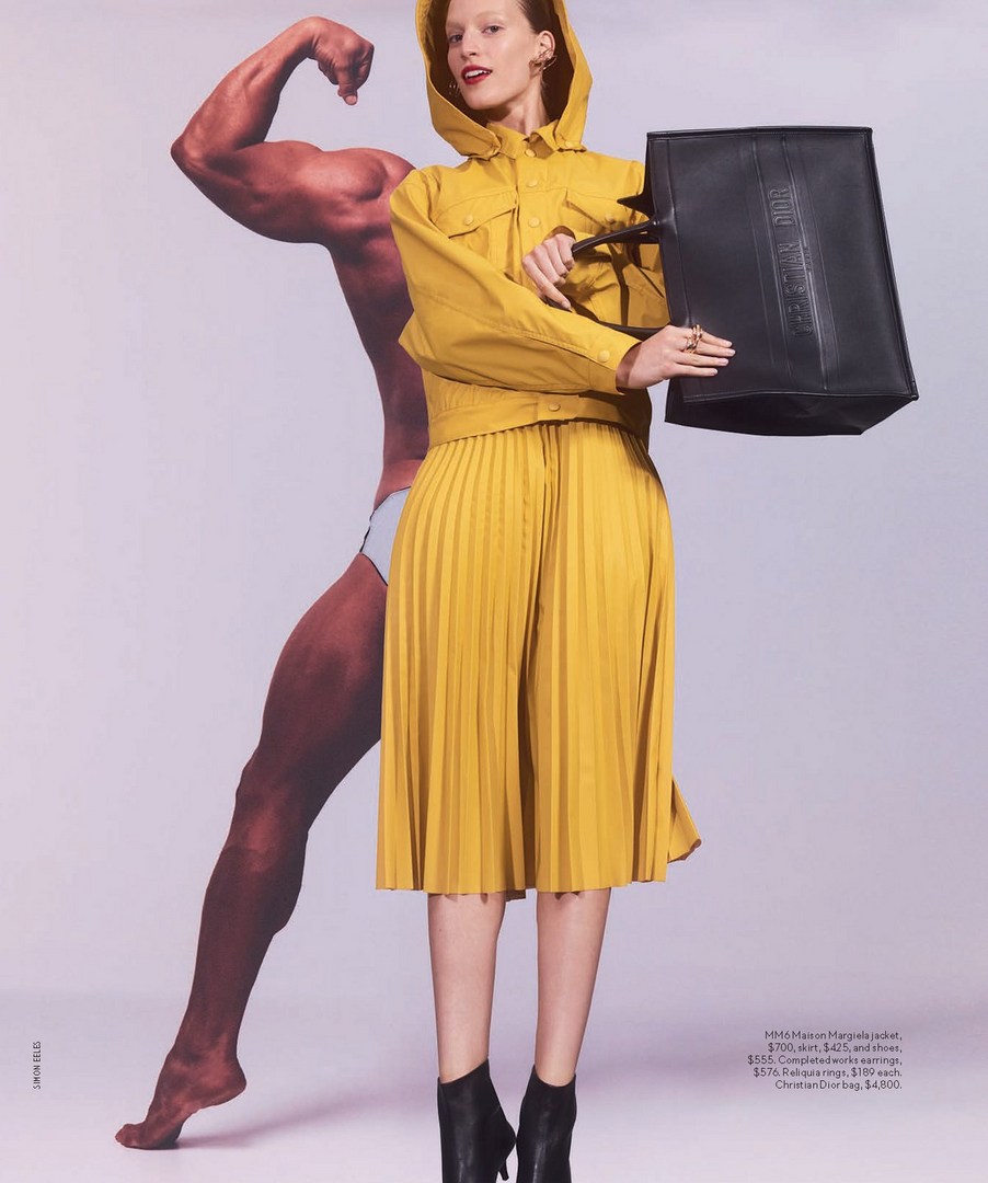 Fashion editorial shot of a woman in yellow hooded jacket, pleated skirt, and black ankle boots, holding a black tote bag.