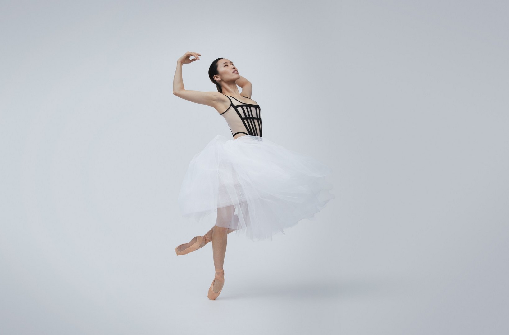 Graceful ballet dancer in black leotard and white tutu, en pointe, against a bright background. Dance and performance captured in a studio shot.