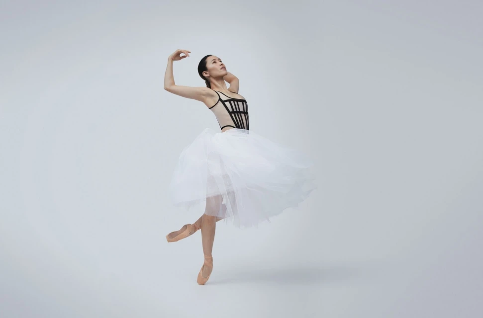 Graceful ballet dancer in black leotard and white tutu, en pointe, against a bright background. Dance and performance captured in a studio shot.
