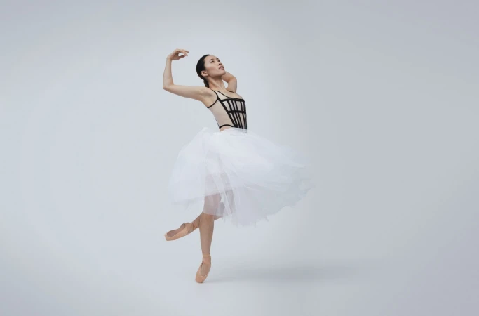 Graceful ballet dancer in black leotard and white tutu, en pointe, against a bright background. Dance and performance captured in a studio shot.