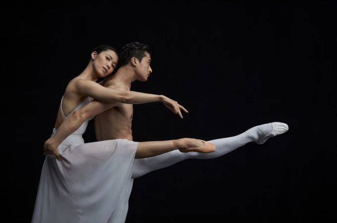 Two ballet dancers in white costumes posing dramatically against a solid black background, styled by Jillian Davison.