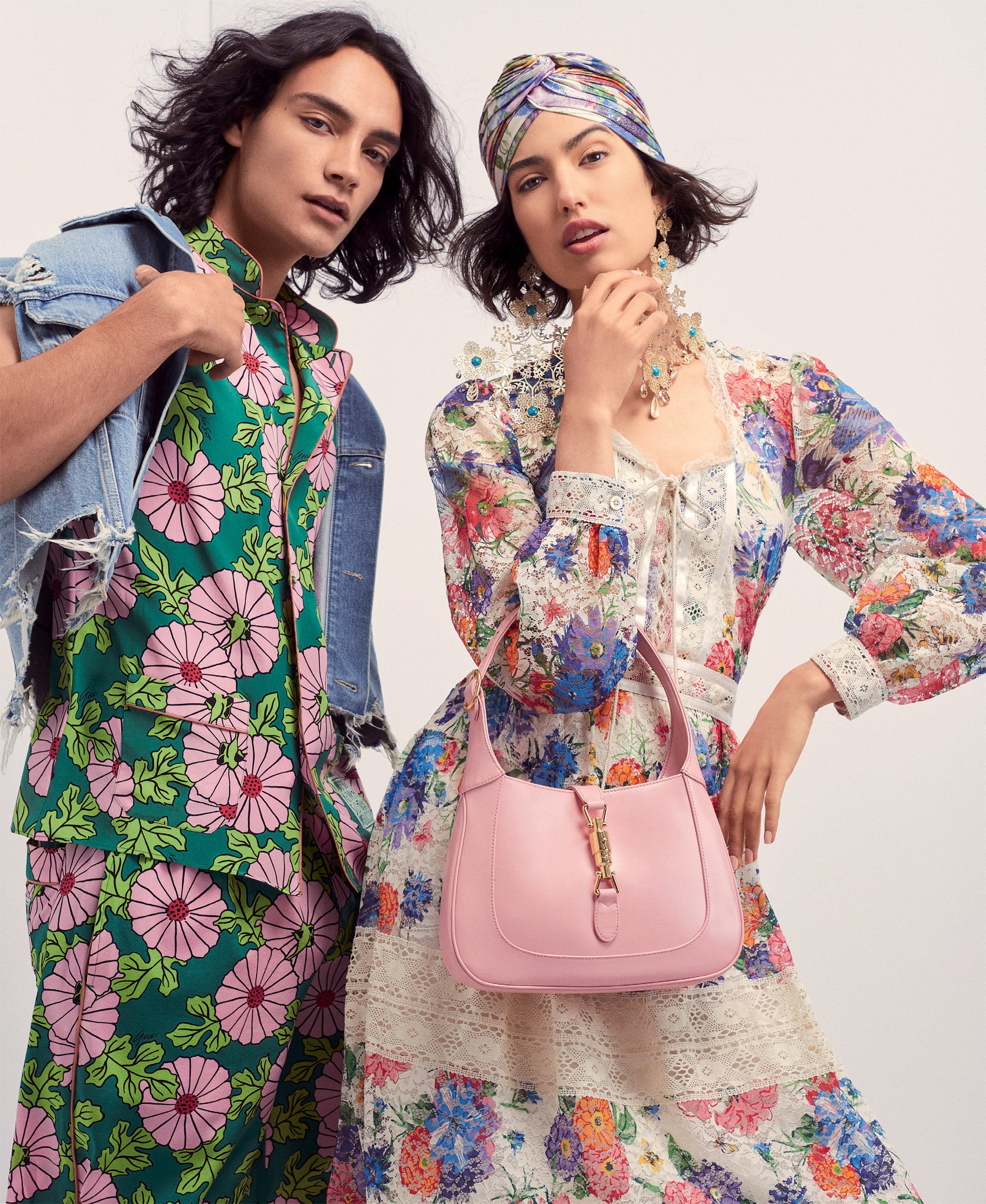 Two fashion models pose in floral print dresses: one in green with a denim jacket, the other in white with a pink handbag.