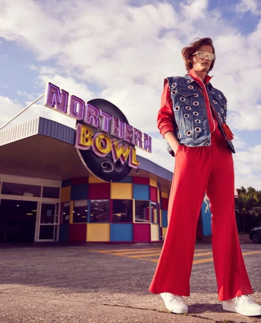 Stylish woman in red tracksuit and denim vest poses in front of vintage bowling alley under bright sky, captured in medium shot.