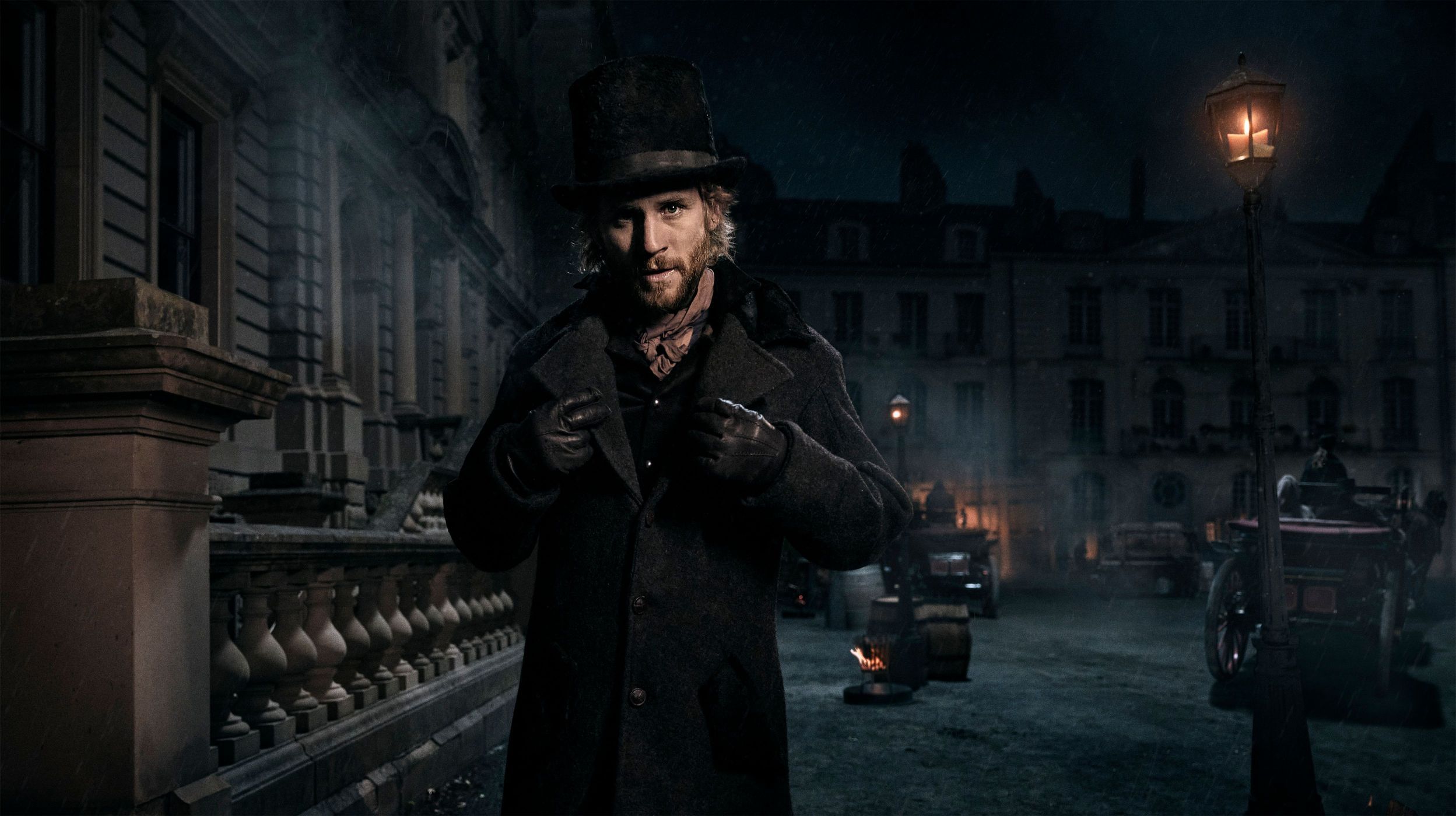 Man in top hat and coat standing on a cobblestone street at night with period buildings and carriages illuminated by a street lamp.