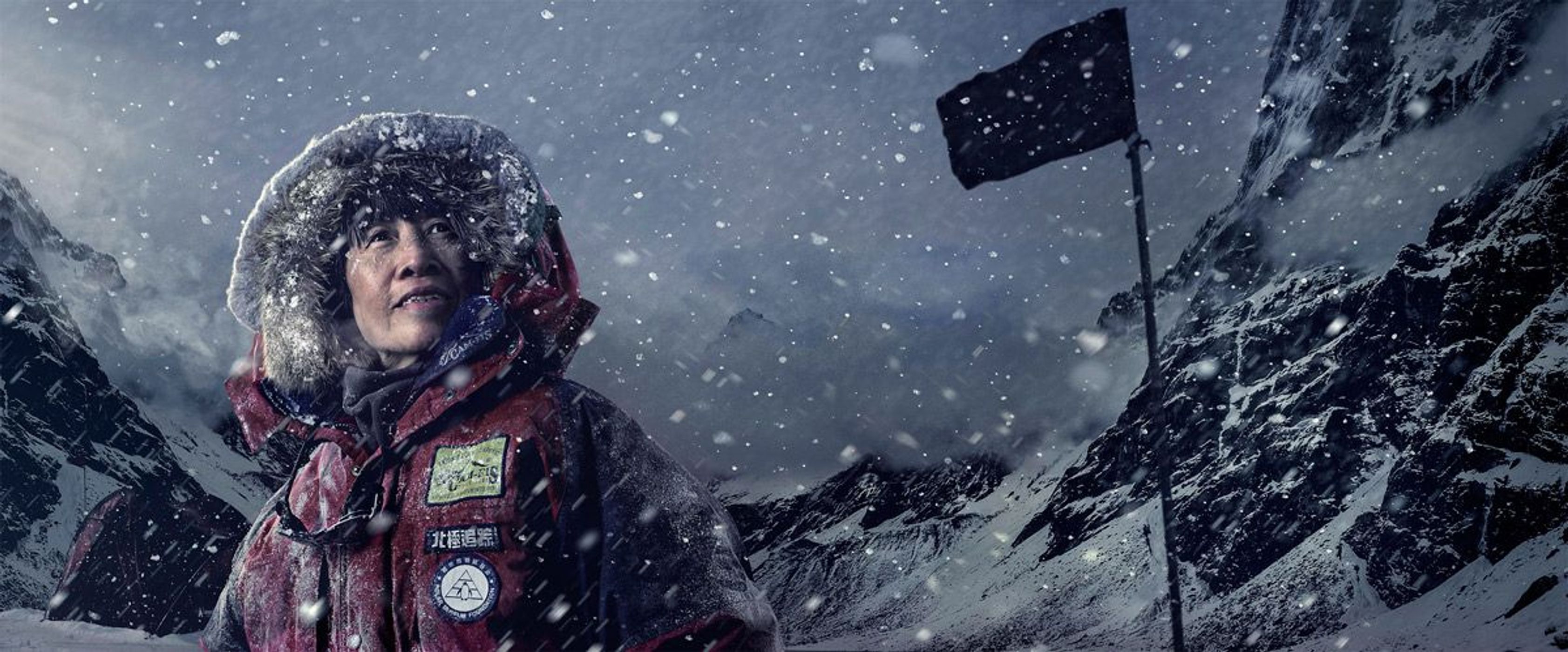 Mountaineer in snow gear amidst a snowstorm, set against snowy peaks and a dark flag atop a mountain. The scene conveys cold and adventure.