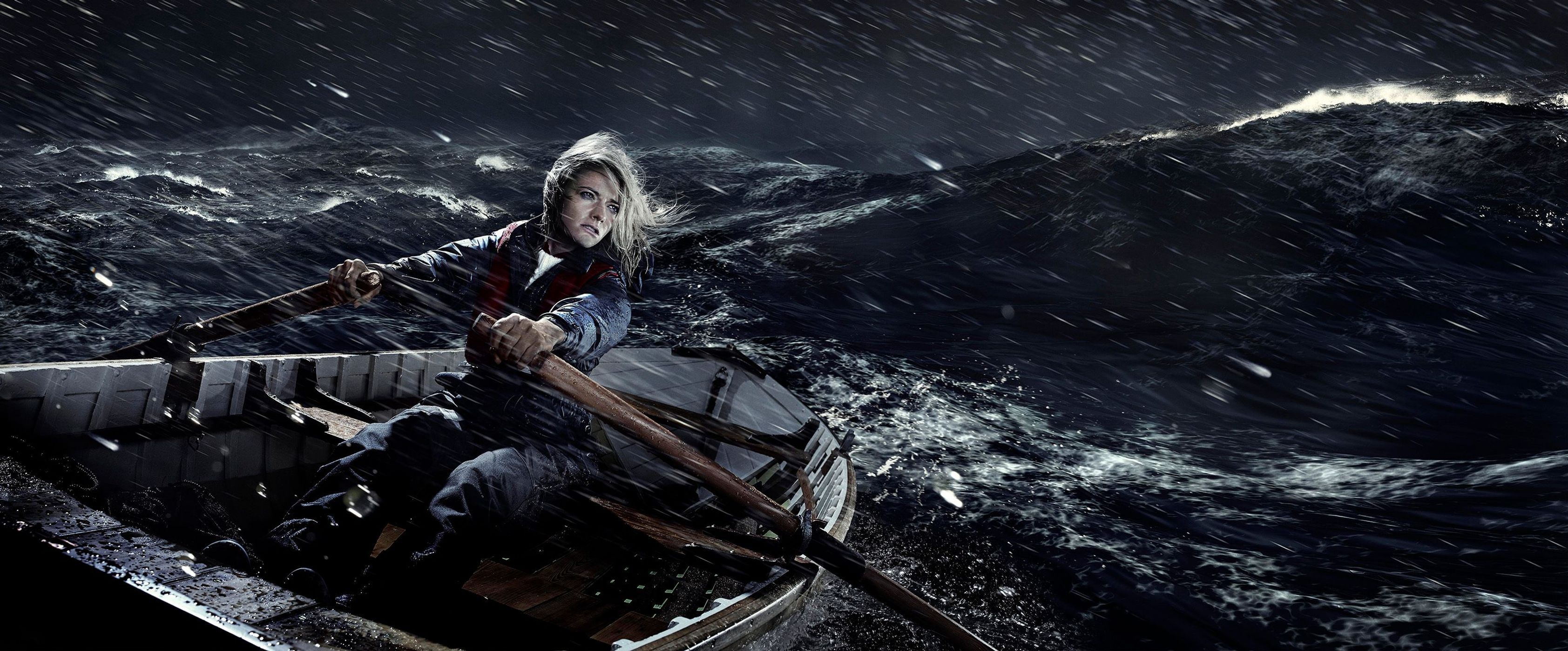 A woman rows a small boat across a dark, choppy sea under a heavy rain. She is wearing a jacket and life vest and looks determined.