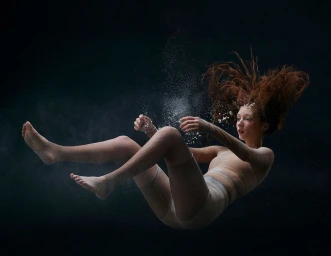 Woman with flowing red hair suspended mid-air in a dark space with particles floating around her