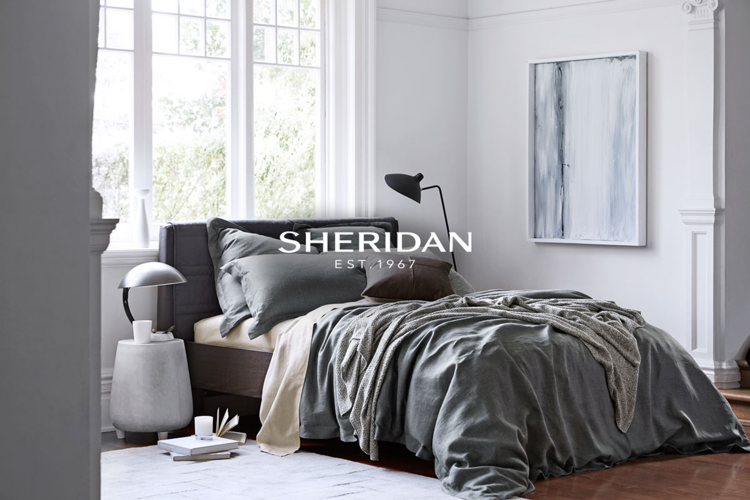 Bedroom interior featuring a grey upholstered bed with pillows and a throw blanket, complemented by a minimalist design and soft lighting.