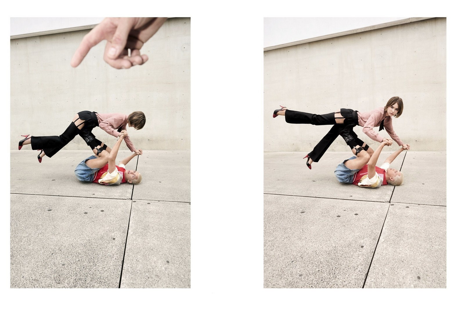 Two women perform an acrobatic pose outdoors with one lying on the ground and the other balancing on her legs, with a hand pointing down.