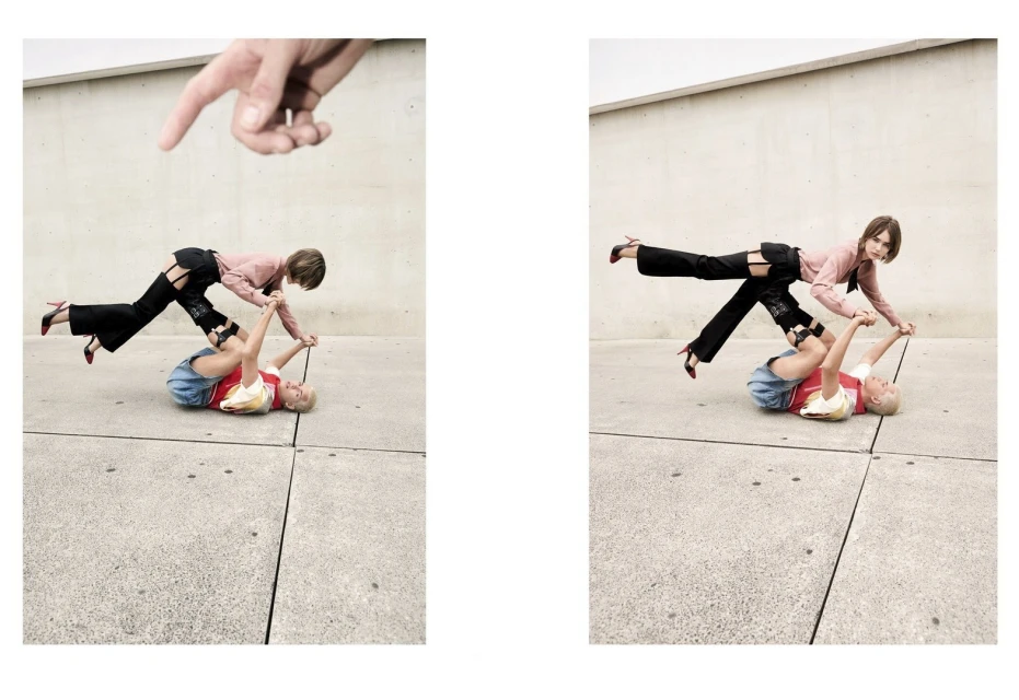 Two women perform an acrobatic pose outdoors with one lying on the ground and the other balancing on her legs, with a hand pointing down.