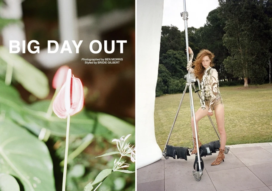 Outdoor fashion shoot with a red-haired woman in patterned top and boots, posing by silver metal studio equipment in a grassy environment.