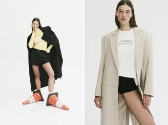 Model wearing traffic cones on feet with oversized black coat and yellow turtleneck against white background