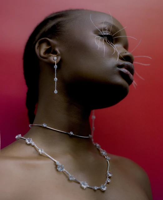 Striking beauty shot of a Black woman wearing jewelry, showcasing white eyelash extensions, set against a vibrant red backdrop.